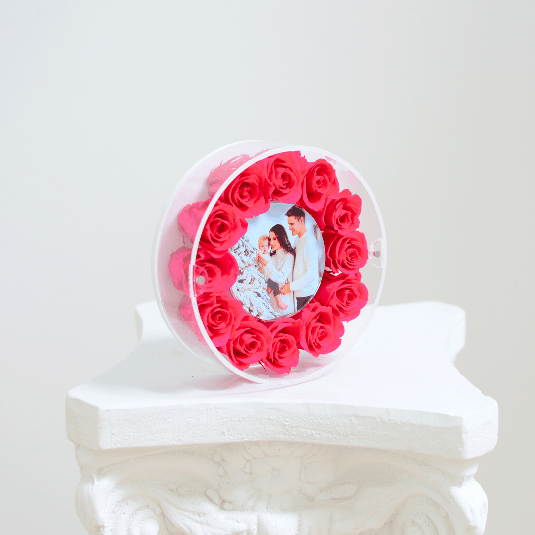 Round acrylic picture frame with fuchsia roses and a photo of a couple and child on a white pedestal.