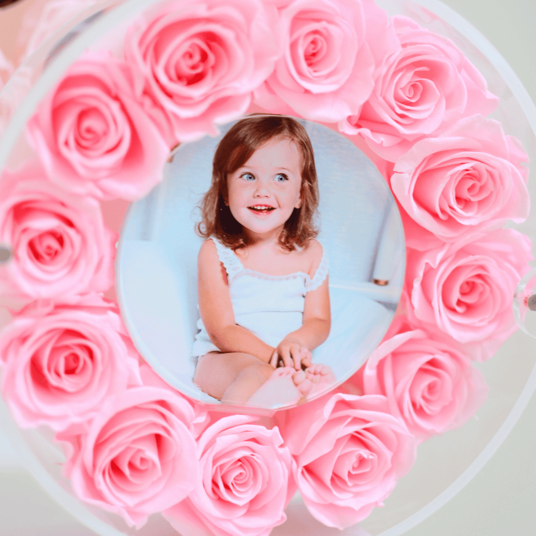 Child in a light blue dress surrounded by pink roses in a circular frame.