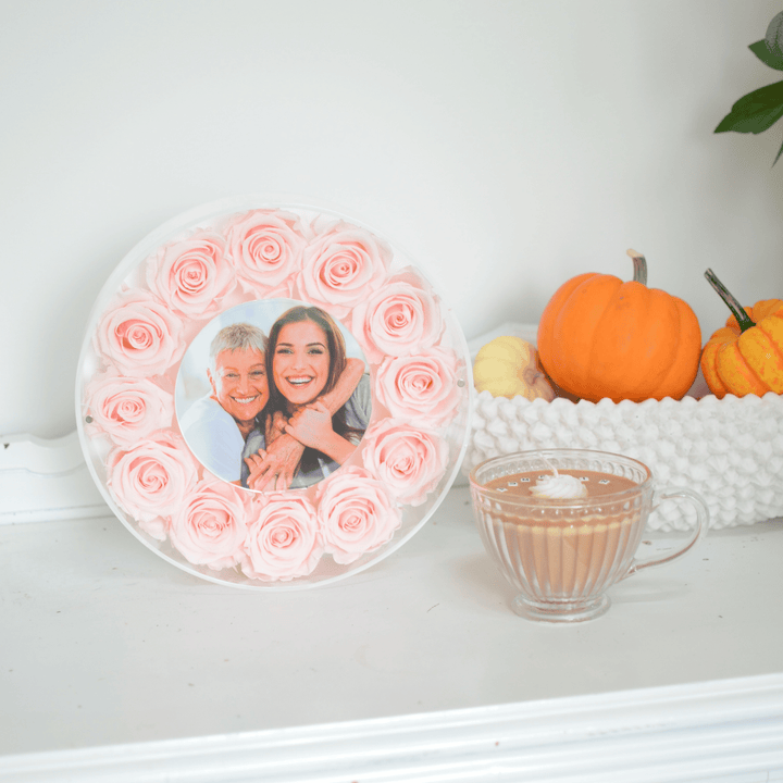 Decorative plate with pink roses and a photo of two people, next to pumpkins and a cup of coffee.