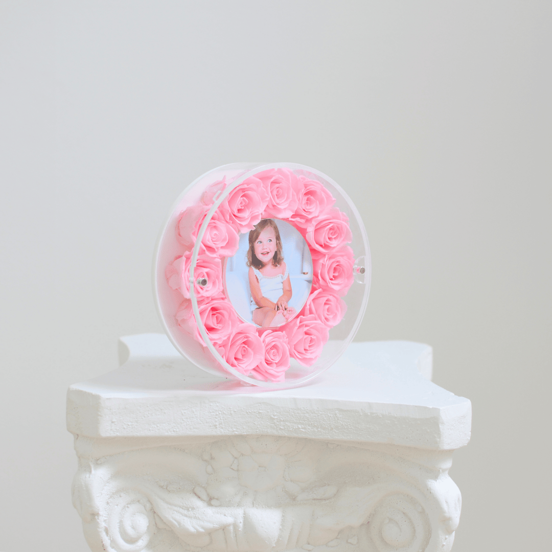 Round picture frame filled with pink preserved roses featuring a photo of a child on a white pedestal.