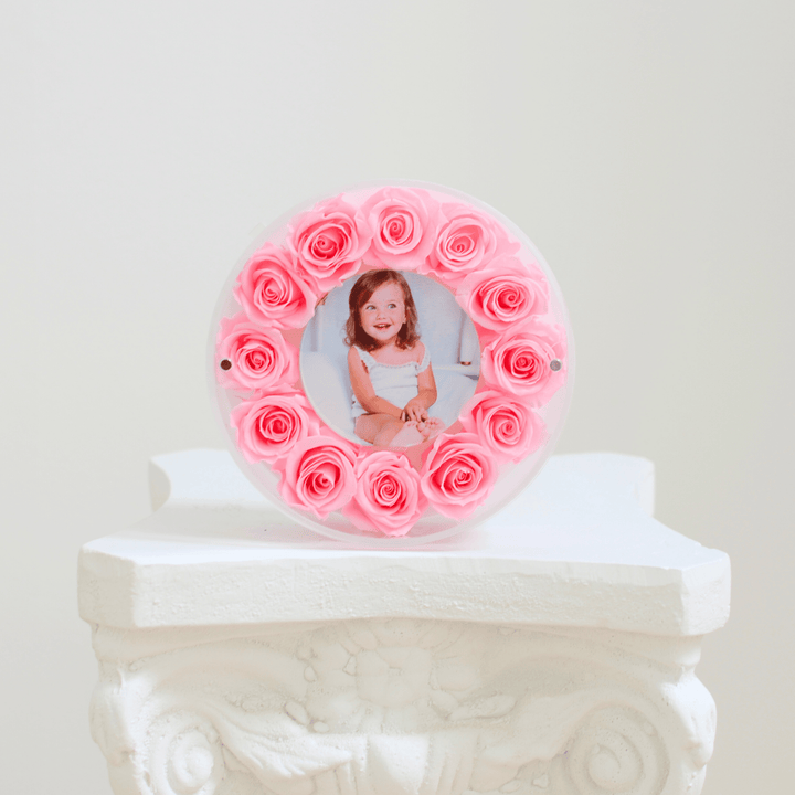 Round photo frame with preserved pink roses on a white pedestal