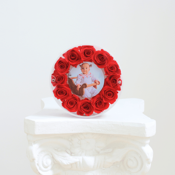 Round red preserved rose frame with a photo of a baby on a white pedestal