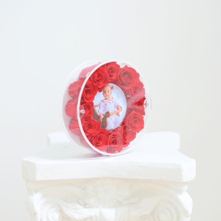 Round acrylic picture frame filled with red preserved roses on a white pedestal